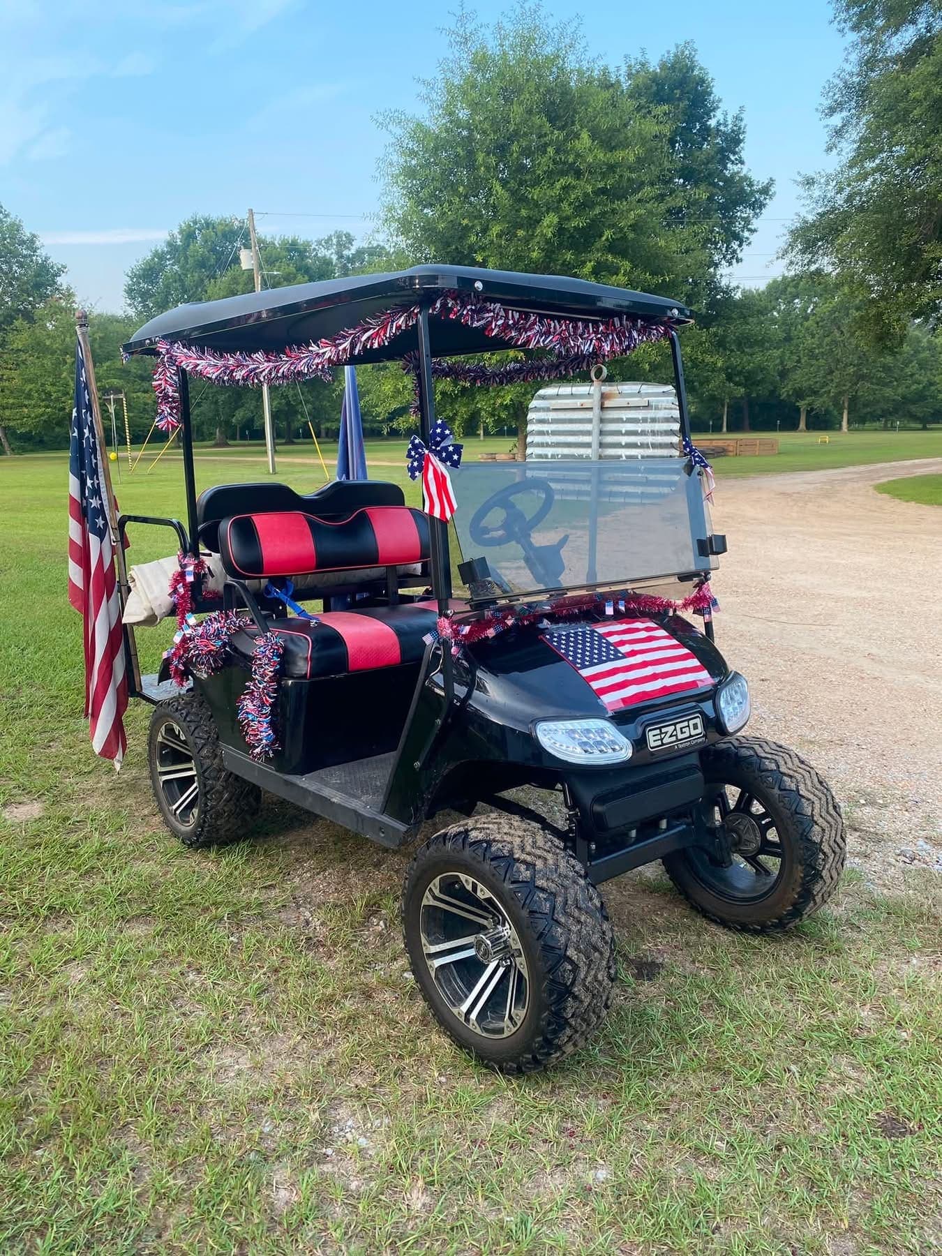 A golf cart parked on the grass, decorated with American flags and red bunting.