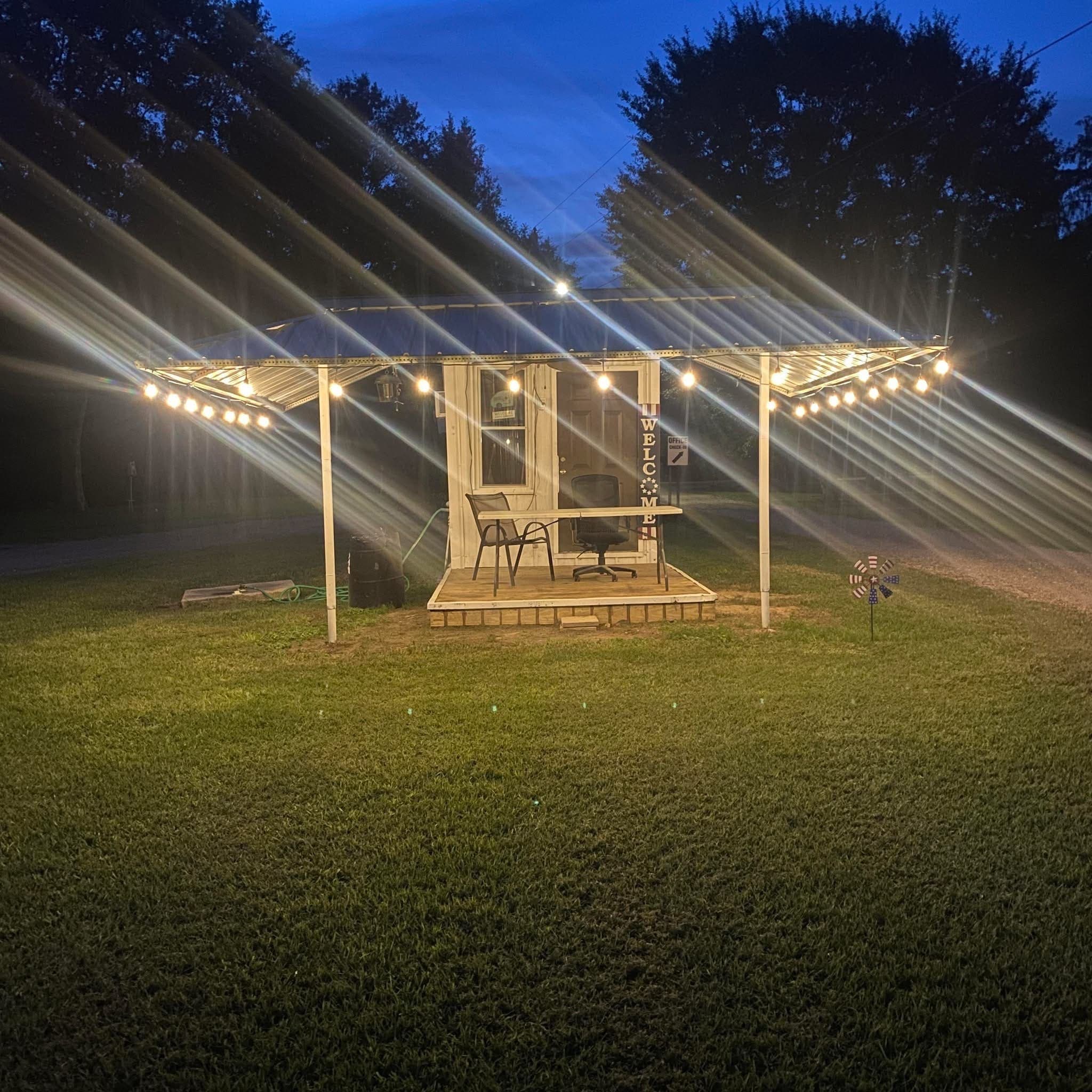 A covered patio hung with string lights, glowing at dusk against the treeline.